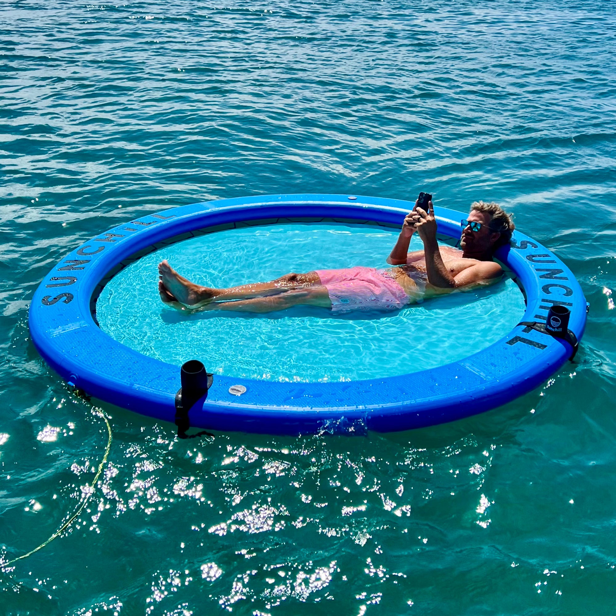 Man lounging in a Royal Blue Sunchill water hammock on clear water.