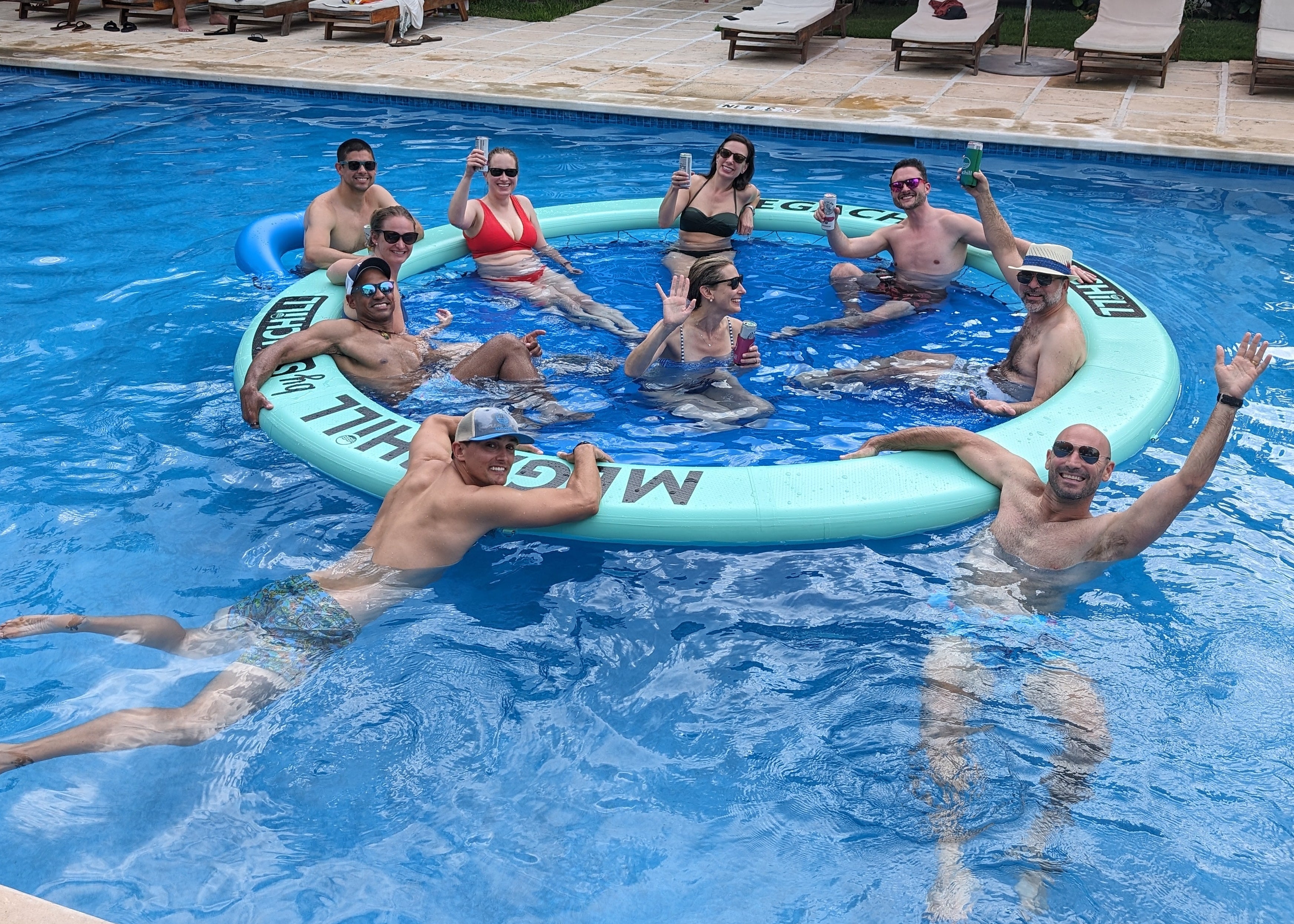 Group of people on an inflatable tube in a pool with lounge chairs around.
