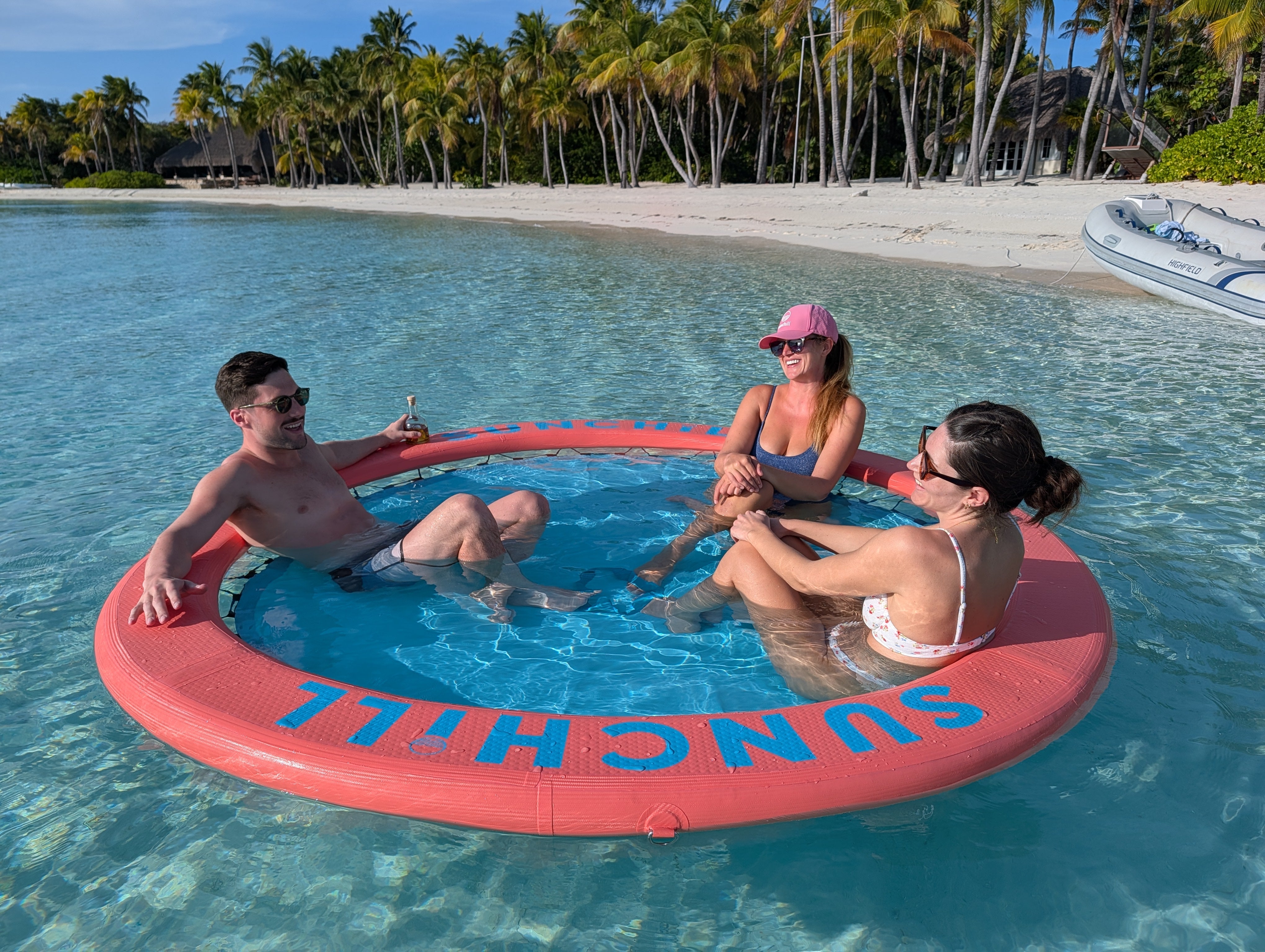 Friends relaxing in a Coral Sea Sunchill water hammock in clear beach water.