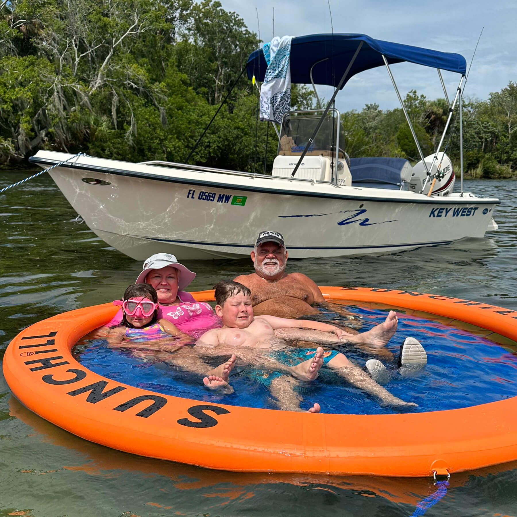 Family relaxing in a Coral Sea Sunchill water hammock near their boat on the lake.